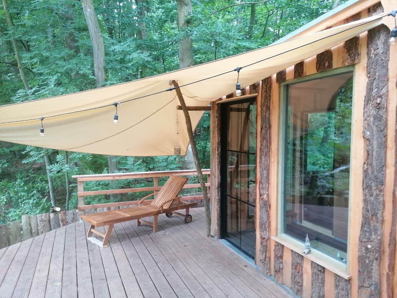 Holzterrasse mit Liegestuhl und Sonnensegel vor der Sauna am Wald